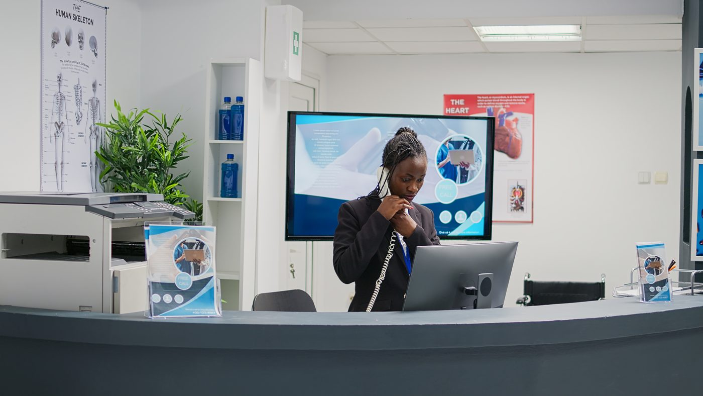 A clinic receptionist answering the phone at a front desk